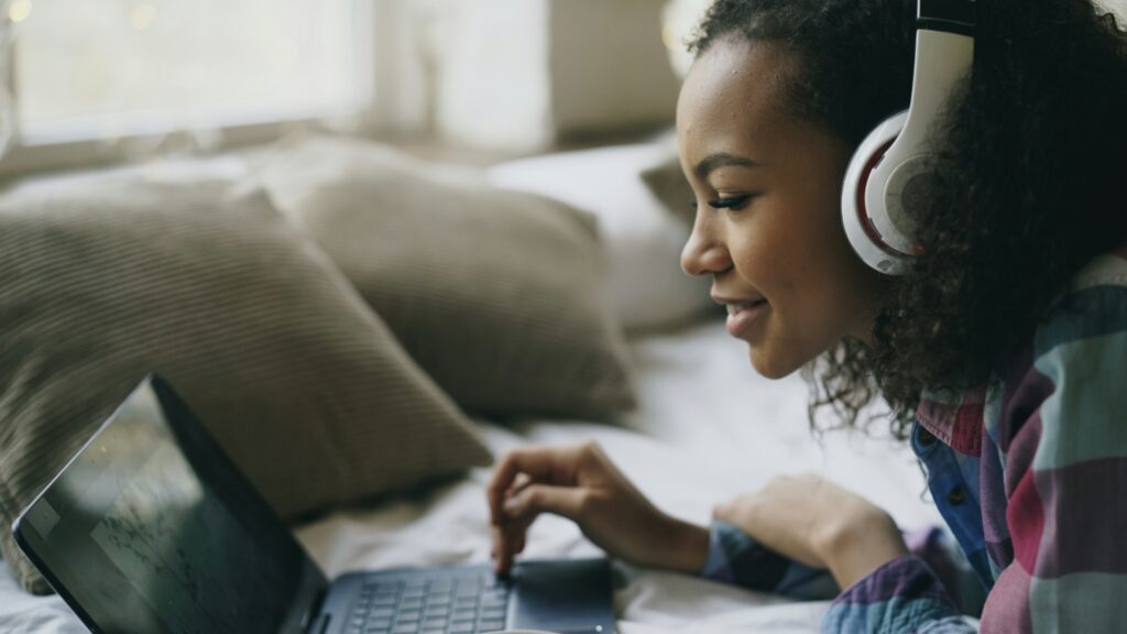 A foreign viewer smiling while watching a Korean drama with headphones on their laptop in a cozy room